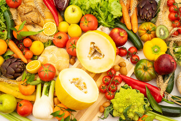 A cut melon on a white wooden board with various fruits and vegetables