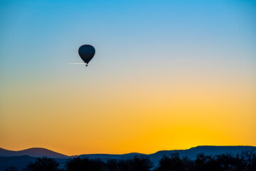 Hot air balloon flying near a aircraft over Cappadocia, orange sky