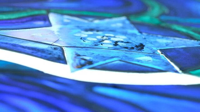An extreme closeup of an artist's hand, brushing the paint lightly on top of a transparent, lit glass, the camera is moving up showing the artist wearing a breathing mask, and then tilting back down.