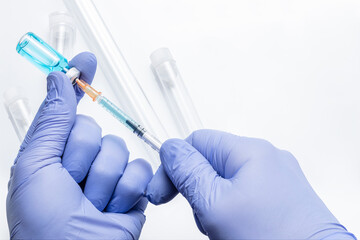 Hands in blue gloves draw medicine from a vial with a syringe on a white background with defocused transparent test tubes