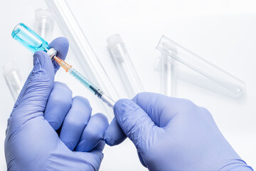Hands in blue gloves draw medicine from a vial with a syringe on a white background with defocused...