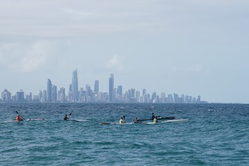 A group of ocean kayaks paddle out to sea together with Surfers Paradise skyline behind them