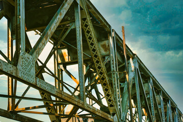 A close up of the girders under a railroad trestle with an dark sky above.