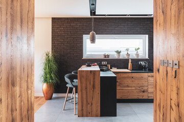Black brick wall in elegant kitchen with wooden island and stylish chairs