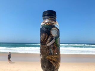 Thrown away beer bottle tops collected in plastic drinks bottle on the beach on a sunny day