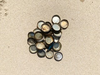 Fototapeta na wymiar Metal bottle lids heaped in a pile on the beach, collected from the sand dunes on the beach