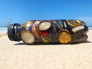 Bottle caps collected from the beach in a thrown away plastic bottle also collected form the beach