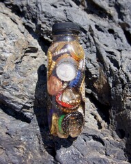 Discarded bottle caps collected in a discarded plastic bottle against a rock cliff