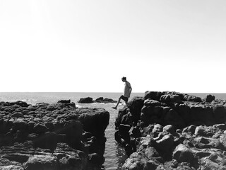 Black and white - stepping across a crack in the rocks with the ocean below