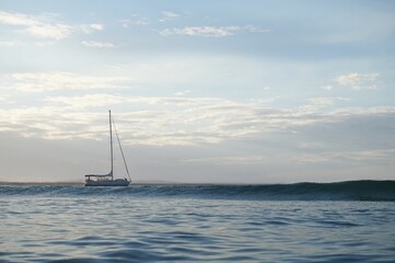 A sailing boat drifts behind an oncoming wave in brilliant light