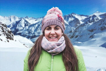 Fototapeta na wymiar Young woman winter portrait in warm clothes against the snowy mountain. Sport activity in the nature and empty copy space.