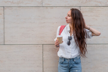 Beautiful woman holds cup coffee her hand, tea, waiting for friends, meeting date. Breakfast lunch break. Casual wear denim shorts, white shirt. In summer granite wall. Free space a copy of text.