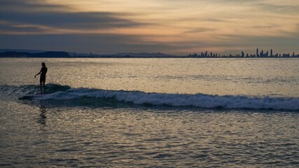 A surfer crusing on a small wave at sunset, Surfers Paradise on the horizon - Australia