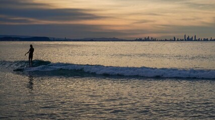 Fototapeta premium A surfer crusing on a small wave at sunset, Surfers Paradise on the horizon - Australia