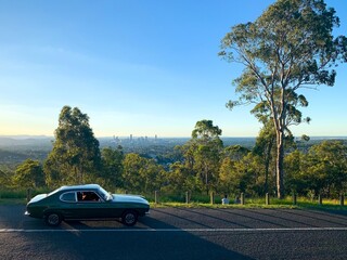 A classic car drives along a road infront of the city skyline - Brisbane, Australia - obrazy, fototapety, plakaty
