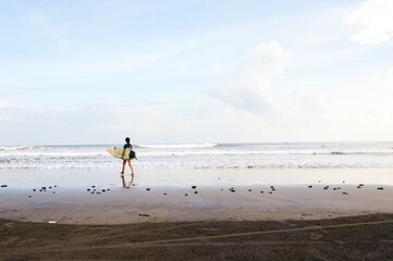 A Japanese tourist walking with a surfboard along a Balinese beach ready for a surf