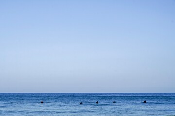 Naklejka premium A minimalistic surf line up. Blue skies and blue waters with a small group of surfers sat on thier boards, Cornwall