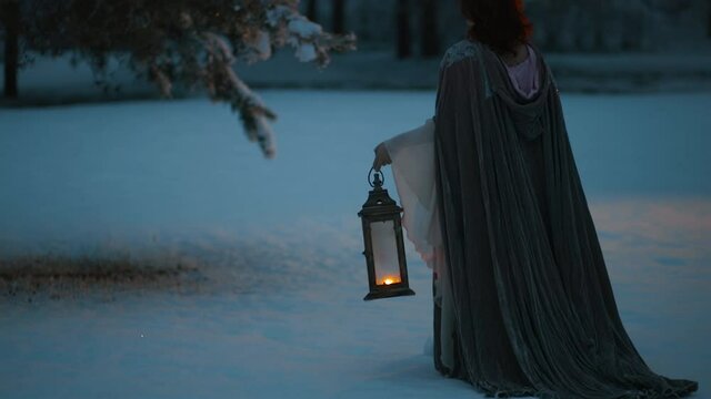 Beautiful fairytale shot of young woman rising vintage lantern emitting warm light. Medieval fantasy concept