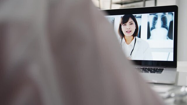 Young Asia female doctor in white medical uniform using laptop talking video conference call with senior doctor at desk in health clinic or hospital. Social distancing, quarantine for corona virus.