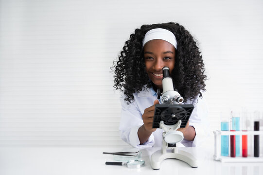 Portrait of happy African American child girl student is learning and test science chemical with colorful liquid by to microscope in laboratory room at school.