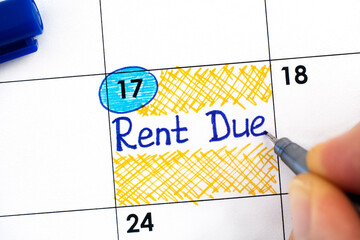 Woman fingers with pen writing reminder Rent Due in calendar.