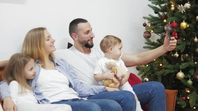 Happy family of four making photo selfie on Christmas time near christmas tree. Beautiful married couple with children using smart phone for taking photos. Happy activity technology lifestyle mobile 