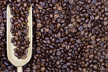 Close up, texture and background of roasted fresh coffee beans with a small wooden scoop in it