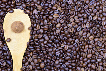 Close up, texture and background of roasted fresh coffee beans on which a wooden spoon lies and a chocolate truffle praline on top