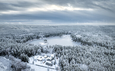 Snowy winter landscape with forest covered in snow. Aerial view over dramatic storm clouds. White scenic countryside.