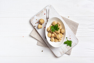 Marinated champignon mushrooms with spice in white bowl on wooden board