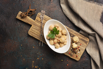 .Marinated champignon mushrooms with spice in white bowl on wooden board