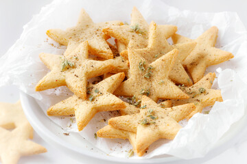 Star shaped savoury shortbread cookies with armesan cheese and black papper sprinkled with aromatic herbs