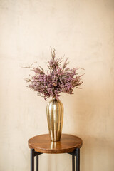 Fototapeta premium Dried Calluna flower in a gold vase on a beige wall background