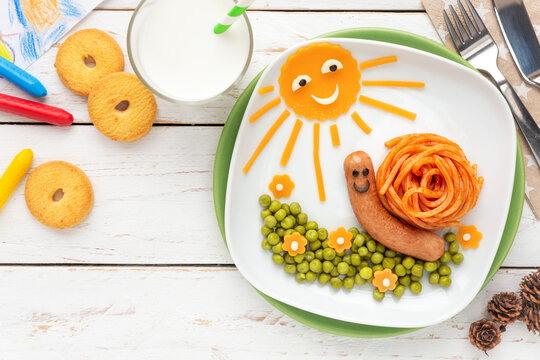Fun food for kids - Cute little snail made of spaghetti and a sausage, served with green peas and cheddar cheese decoration