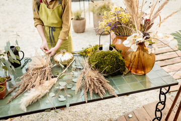 Female making compositions of dried and fresh flowers and herbs on the green table outdoors. Florist, gardener or decorator composing floral decoration concept. Close-up shot