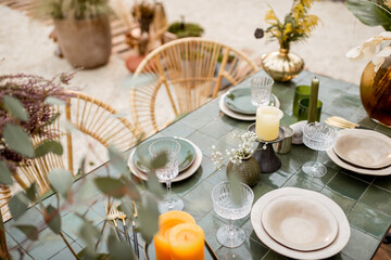Festively decorated tablescape in green tones with candles, herbs and flowers in a natural Boho style outdoors