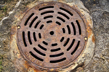 Weathered large manhole cover showing texture and color and abstract design
