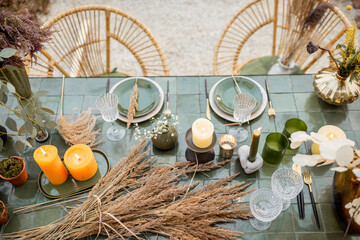 Tablescape of a festivly decorated romantic lunch place in green tones with candles, herbs and flowers in a natural Boho style outdoors. View from above