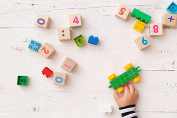 Top view of a child's hands playing with children's educational toys, colorful cubes, bricks on a white wooden background. Developing concept