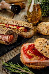 Still life composition of delicious hot dogs and sandwiches with different toppings and dried onion on the dark background