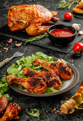 Still life of a plate of roasted or grilled chicken legs with golden brown crust served on a black plate with fresh salade and souce