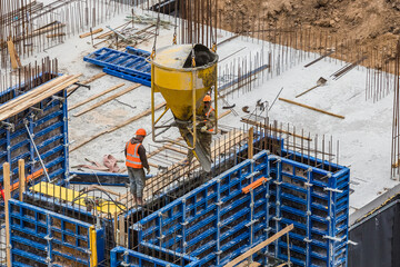 Concreting work at the construction site. Сonstruction workers pour liquid concrete from cement concrete hopper to fromwork installation.