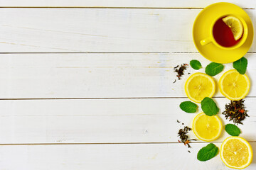 Background of yellow cup of tea, lemon and mint on a white wooden background.