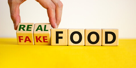 Real or fake food symbol. Male hand flips wooden cubes and changes words 'fake food' to 'real food'. Beautiful yellow table, white background. Healthy lifestyle and real or fake food concept.