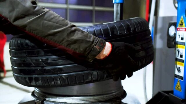 Close up of worker hands changing tire at the car service. Footage. Car mechanic is changing a tyre in a garage with the professional equipment.