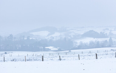 Fototapeta na wymiar Misty snow covered hills beyond the fields