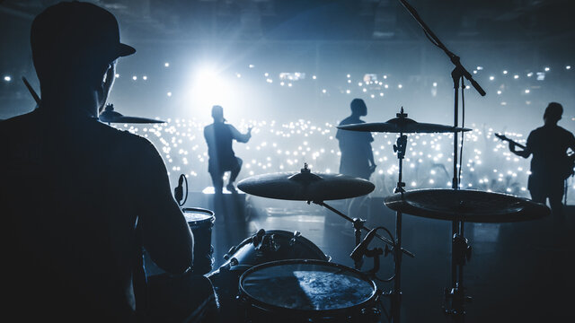Music band group silhouette perform on a concert stage.  
silhouette of drummer playing on drums
audience holding cigarette lighters and mobile phones