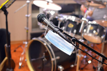 medical mask hangs from a microphone on a blurry drum kit background