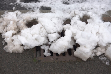 11 - Heavy snow melts over a metal curbside drain, giving flood risk