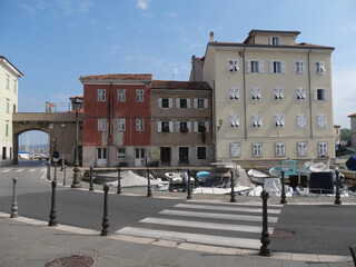 Naklejka premium Mandracchio in Muggia : it is a small harbor inside the village and surrounded by ancient walls and colorful buildings. There are colored boats moored and reflected in the water.